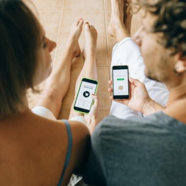 A couple using smartphones for online shopping while relaxing indoors on a tiled floor.