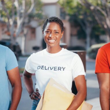Three delivery team members holding packages with smiles outdoors, showcasing teamwork and service.